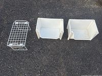 Two white plastic bins and one white metal wire rack laid out on pavement
