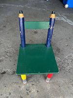 Front view of chair showing green seat, blue pencil back posts, yellow and red pencil front legs