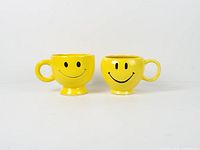 Front view of both yellow smiley face mugs