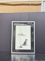 Framed black and white ink reproduction print of dog under tree, portrait orientation, silver metal frame with glass