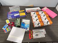 Entire lot displayed on tabletop showing binder clip boxes, envelopes, label pack, page flags, index cards, utility knife, push pins and staples
