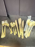 All pieces of the 16-piece gold-tone flatware set laid out showing forks, knives, teaspoons and wrapped tablespoons