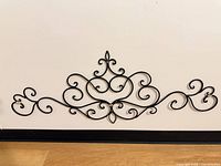 Full view of black wrought iron scrollwork wall decor against wall and floor for scale