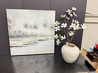 Canvas art beside ceramic vase containing white silk flowers