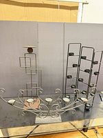 All three candle holders grouped: scrollwork candelabra, ladder tealight holder, geometric pedestal stand