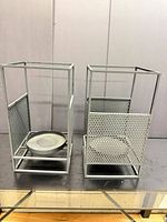 Front view of both black metal lanterns showing perforated panels and removable candle tray
