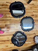 Three black quatrefoil wall mirrors placed on floor