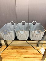 Front view of three gray woven-look plastic baskets aligned side by side on glass table