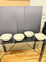 Four white scalloped serving bowls displayed on glass table