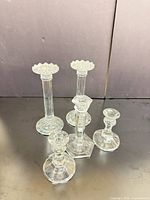 Front view of all five clear pressed glass candlesticks showing varied heights and styles