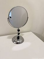 Front view of round chrome vanity mirror with black accented stem on white surface