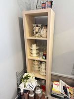 Front angled view of tall narrow light wood bookcase with three shelves and contents for scale