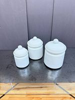Front view of three white ceramic canisters with lids