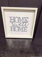 Front view of square white wooden wall sign with raised grey "Home Sweet Home" text