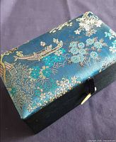 Closed box showing embroidered silk top with boat scene