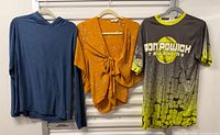 All three tops hanging: blue hoodie, orange floral blouse, grey/yellow jersey