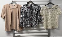 Overall view of three tops hanging: beige cardigan, zebra jacket, lace blouse