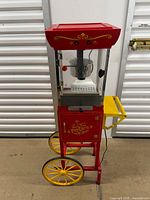 Front view of popcorn machine showing kettle, glass panels, wheels and side tray