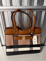 Front view of structured colorblock handbag showing gold-tone bar and attached tag