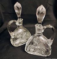 Two clear cut crystal cruets with stoppers on black background
