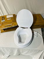 Raised toilet seat displayed with both product boxes