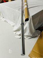 Full view of chrome barbell bar next to shipping tube