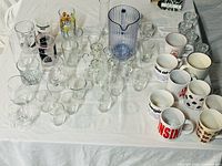 Full lot overview showing mugs, tumblers, shot glasses, snifters and blue pitcher