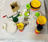 Full lot layout showing apple peeler, rotary grater, drums, citrus juicer, storage container, stackable plates, bowls, and mugs