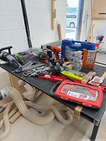 Wide view of assorted hand and power tools on tabletop including socket set, cordless drill, reciprocating saw, bit sets and hardware