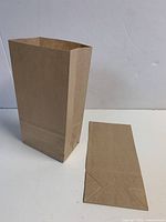 Brown paper bag standing open beside one folded flat bag