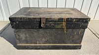 Front view of black wood tool chest showing hasp latch, yellow paint drips, general wear