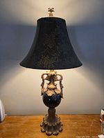 Full view of lamp on table showing base, body, shade, finial