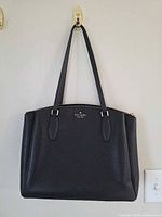 Front view of black pebbled leather Kate Spade tote bag hanging on hook