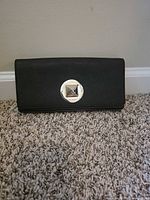 Front view showing black saffiano clutch and square metal turn-lock