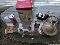 Overall lot on glass table showing tins, camera, flash, Pepsi can, jars, knife, arrowhead, pins