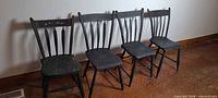 Four wooden arrowback chairs lined against wall