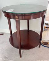 Full view of round mahogany end table with glass top and lower shelf
