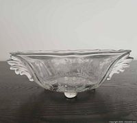 Side profile of clear crystal bowl showing winged handle, etched pattern, footed base