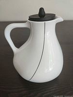 Side view of white porcelain teapot with black lid showing handle, spout and accent line