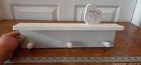 Front view of coat rack showing three pegs, shelf top, and owl ornament