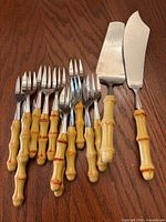Entire 14-piece set laid out: 12 dessert forks, 1 cake server, 1 pie server, showing faux bamboo handles and stainless ends