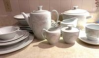 Grouping of porcelain dinnerware showing floral patterned coffee pot, creamers, sugar bowl, soup tureen, stacks of plates and bowls