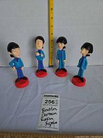 Four Beatles resin figurines on red bases with measuring tape for height reference