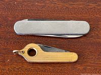 Both pocket knives side by side closed on wood surface