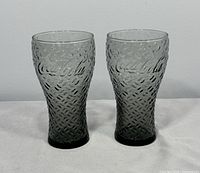 Two smoked grey Coca-Cola glasses side by side