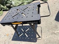 Overall view of DeWalt folding workbench standing on ground, shows plastic top, metal legs, carry handle