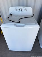 Front view of GE top-load washing machine with power cord visible