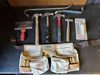 All items laid out: tool belt, hammers, pry bars, scraper, trowel