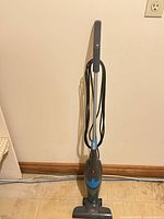 Full view of Bissell gray/blue corded upright steam mop standing against wall showing handle, power cord, and steam head