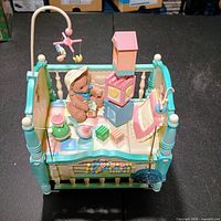 Front angled view of crib-shaped Enesco music box with teddy bear, blocks, mobile and abacus detail
